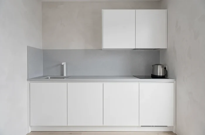 Cuisine épurée avec seulement deux matériaux visibles — laque blanche et quartz gris clair — réduisant la complexité visuelle pour agrandir l'espace perçu